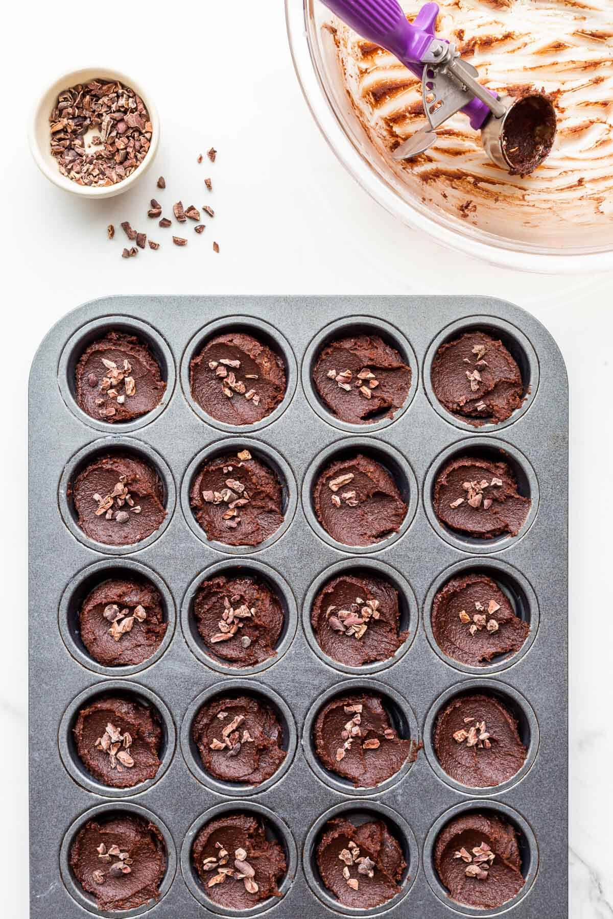 Garnishing chocolate financiers with cocoa nibs before baking them.