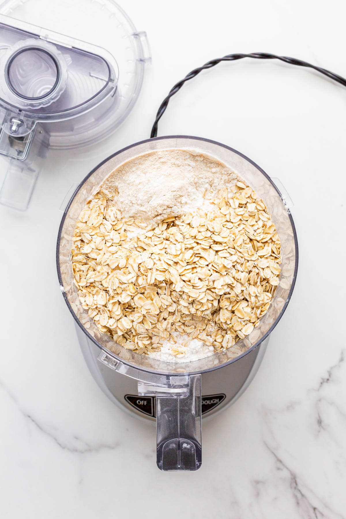 Dry ingredients including rolled oats in food processor bowl to be processed into flour.