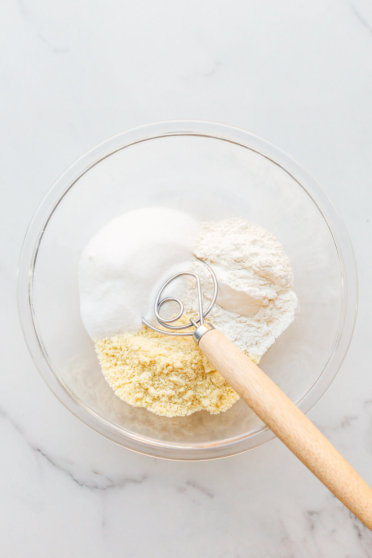 Whisking dry ingredients in a glass bowl to make raspberry financiers cakes, including flour, sugar, and ground almonds.