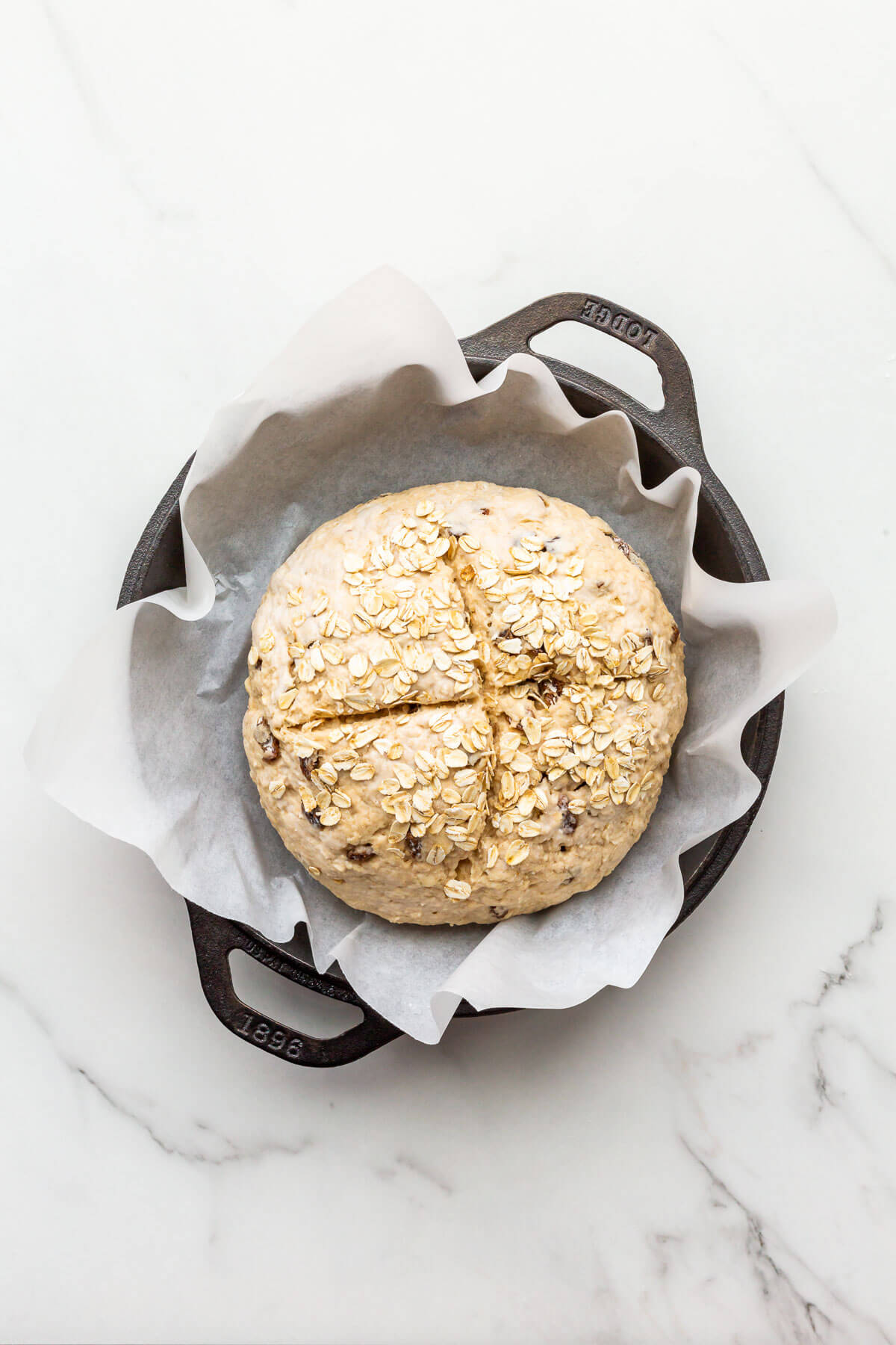 Soda bread with oats and raisins before baking in a parchment-lined cast iron skillet.