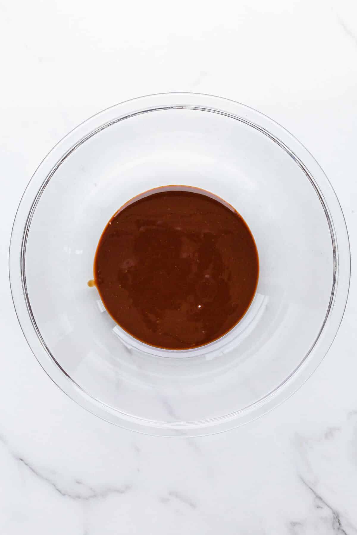 A glass bowl of melted chocolate and butter to make chocolate frosting.