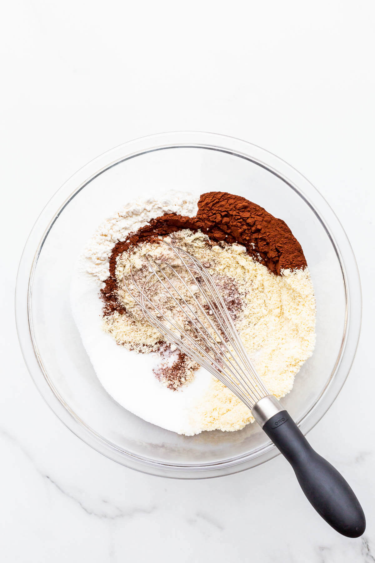 Whisking dry ingredients in a glass bowl to make chocolate financiers cakes.