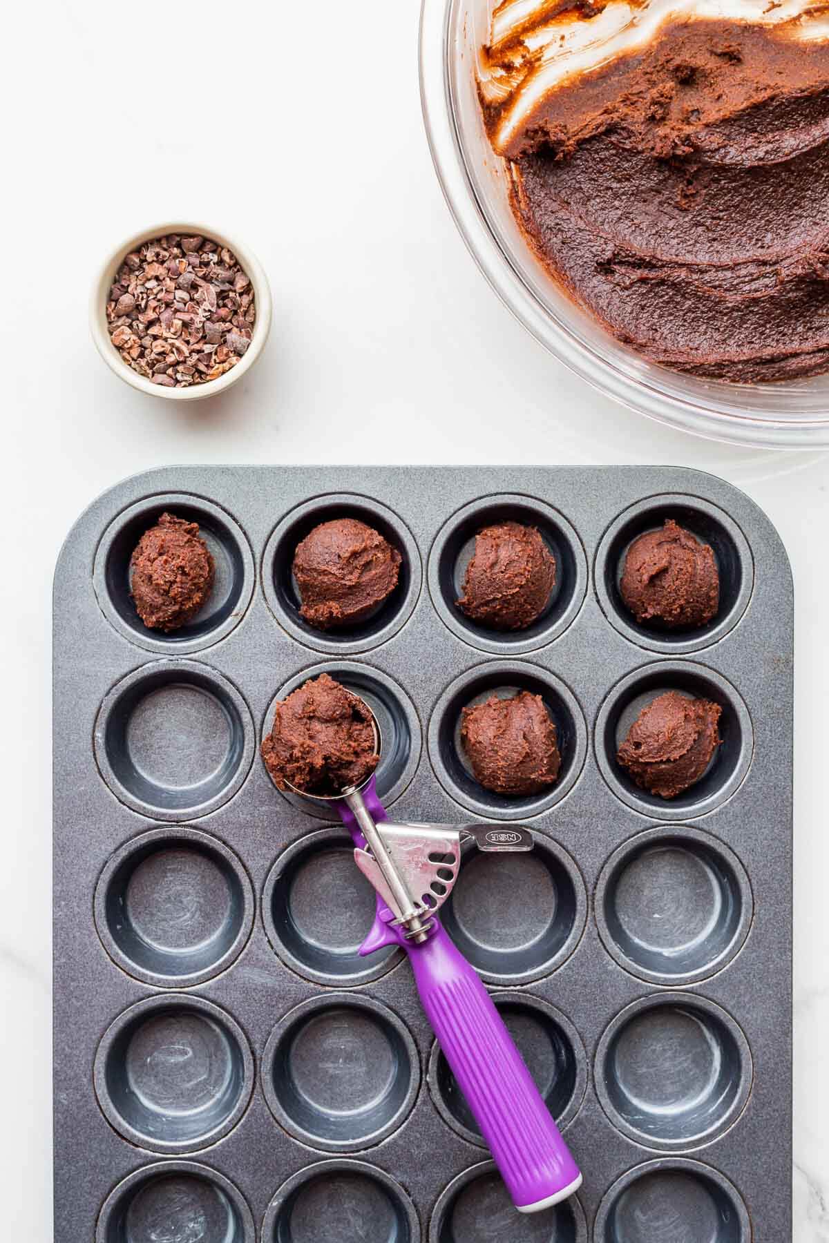 Portioning chocolate batter into buttered muffin pan with a cookie scoop (disher) to make financier cakes.