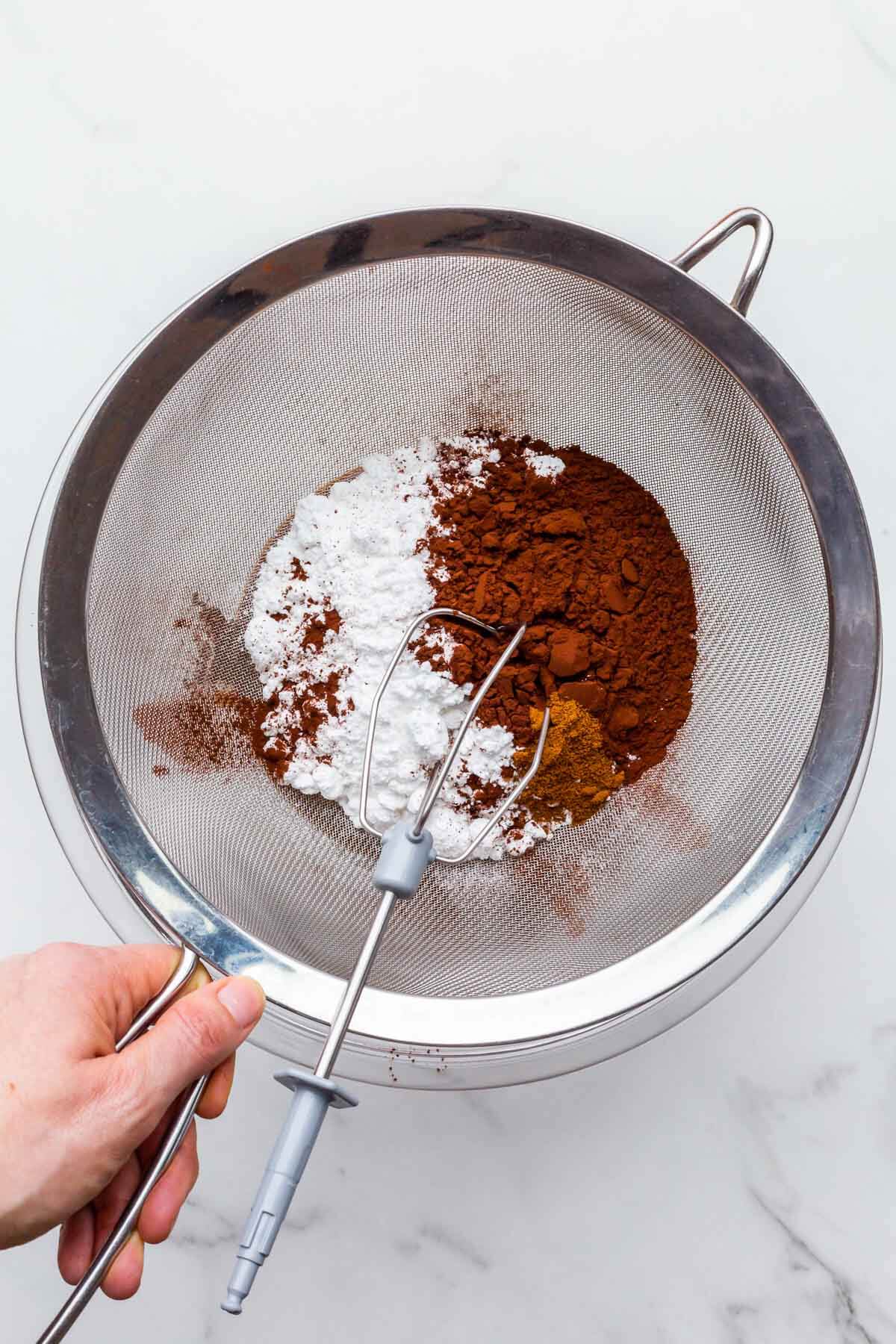 Sifting icing sugar and cocoa powder through a strainer to remove lumps to make smooth and creamy chocolate frosting.