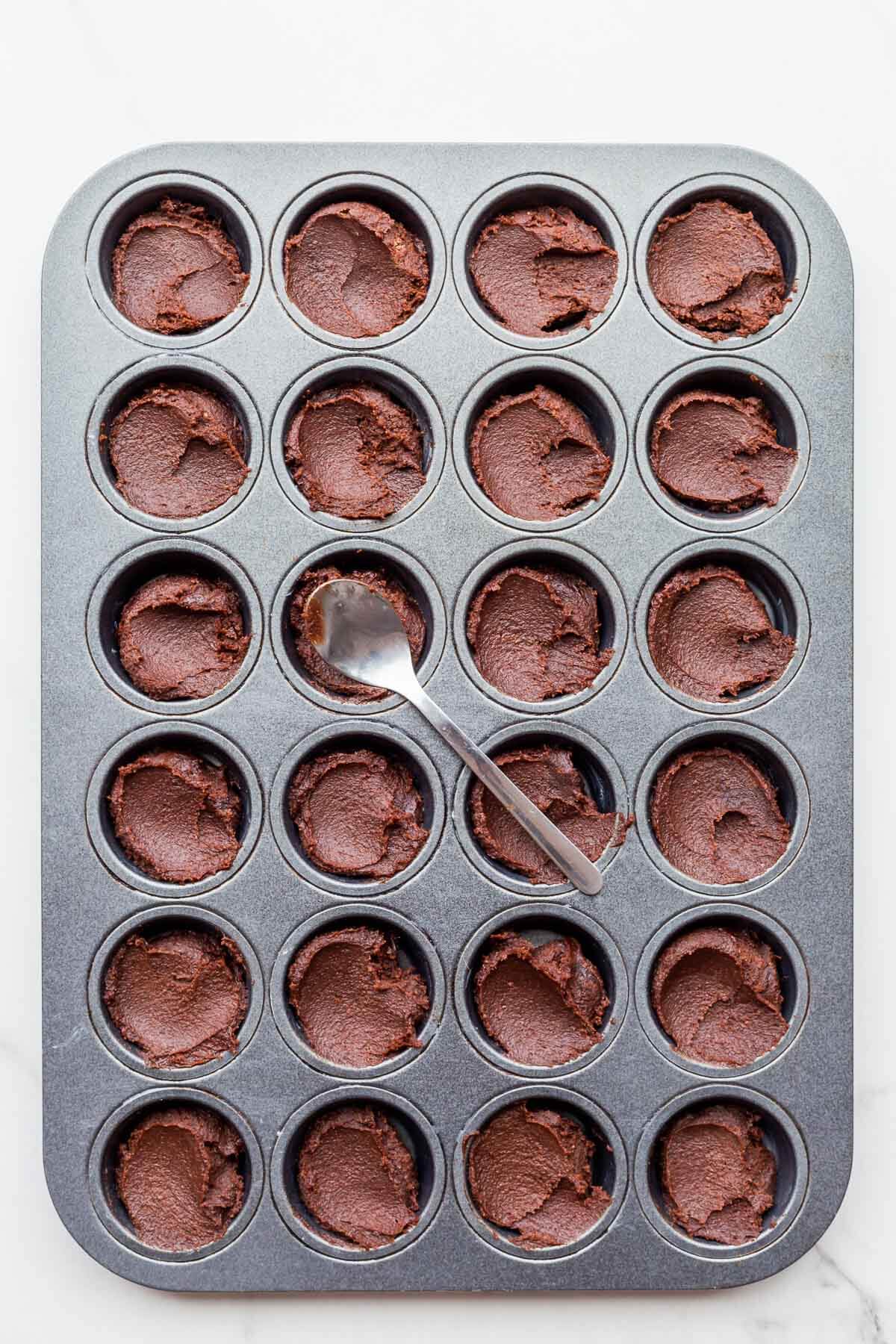 Smoothing the tops of financier batter in a muffin pan with the back of a small spoon before baking.