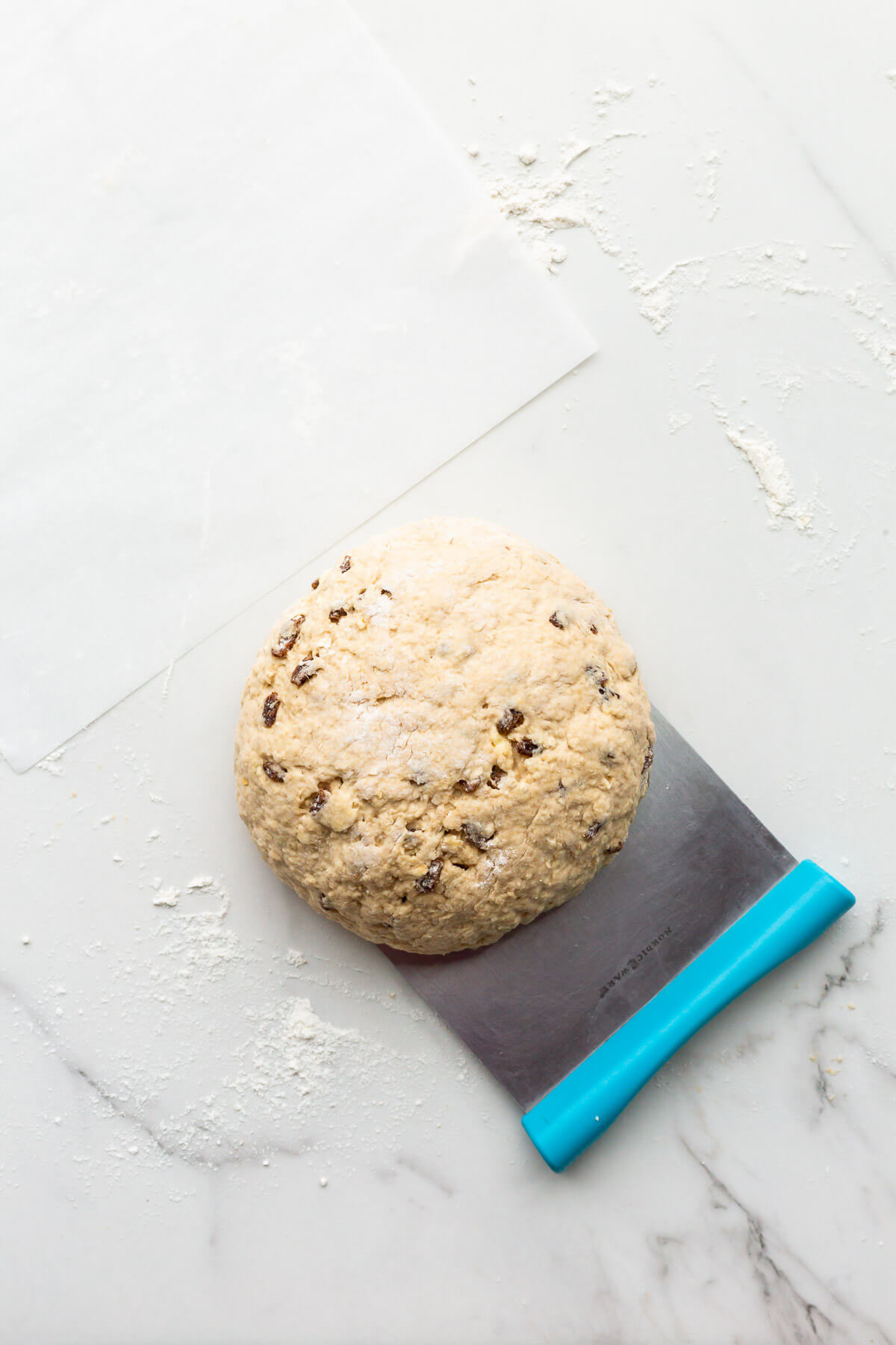 Using a bench scraper to lift sticky Irish soda bread dough to transfer it to a pan to bake it.