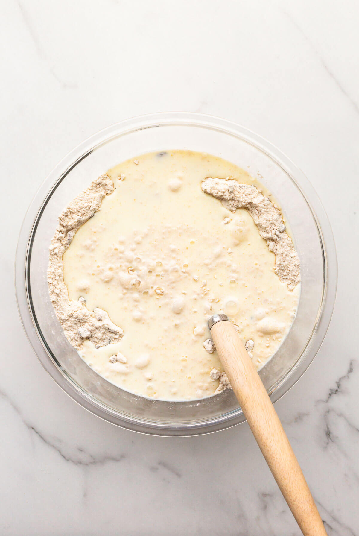 Whisking wet ingredients in a glass bowl with dry ingredients to make soda bread.