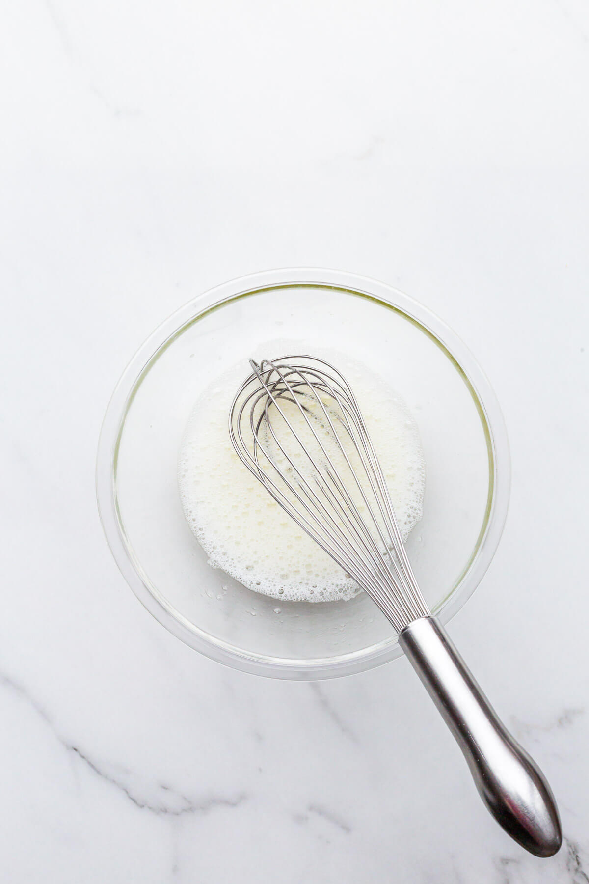 Whipping egg whites in a glass bowl until very frothy and foamy.
