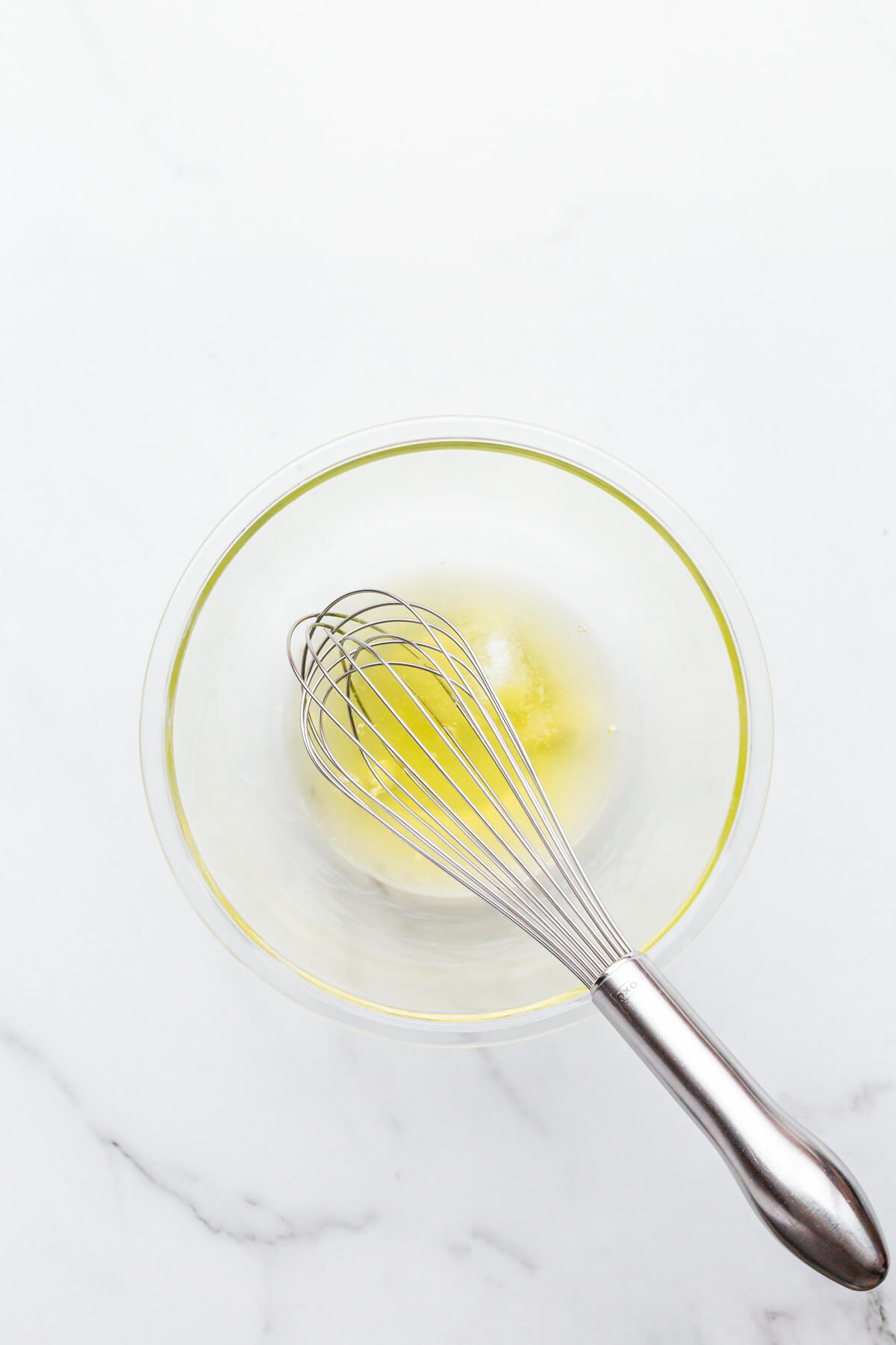 Egg whites in a glass bowl with a whisk that are ready to be whipped to make financiers.