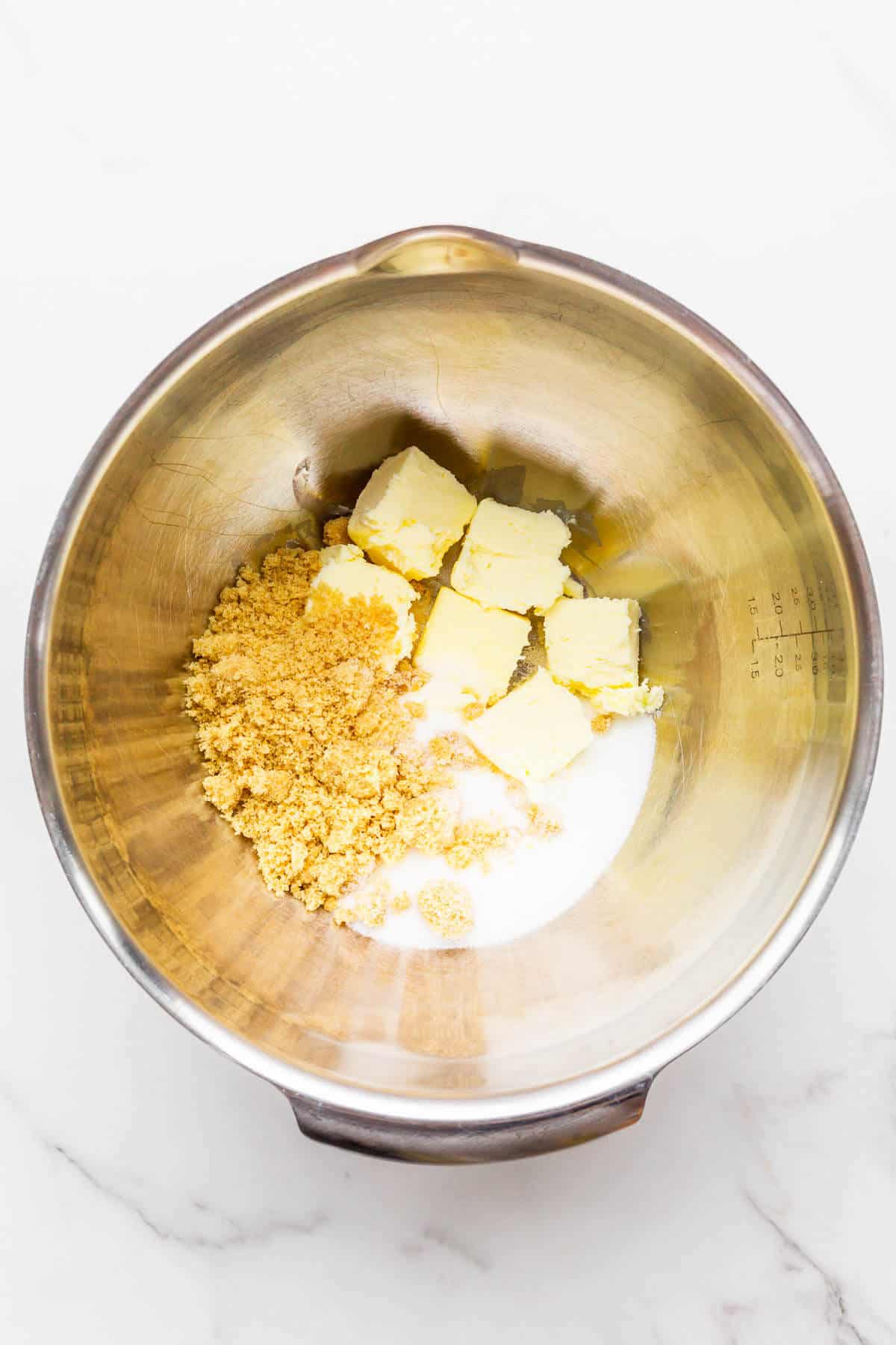 Cubes of softened butter, brown sugar, and granulated sugar in a mixing bowl ready to be creamed.