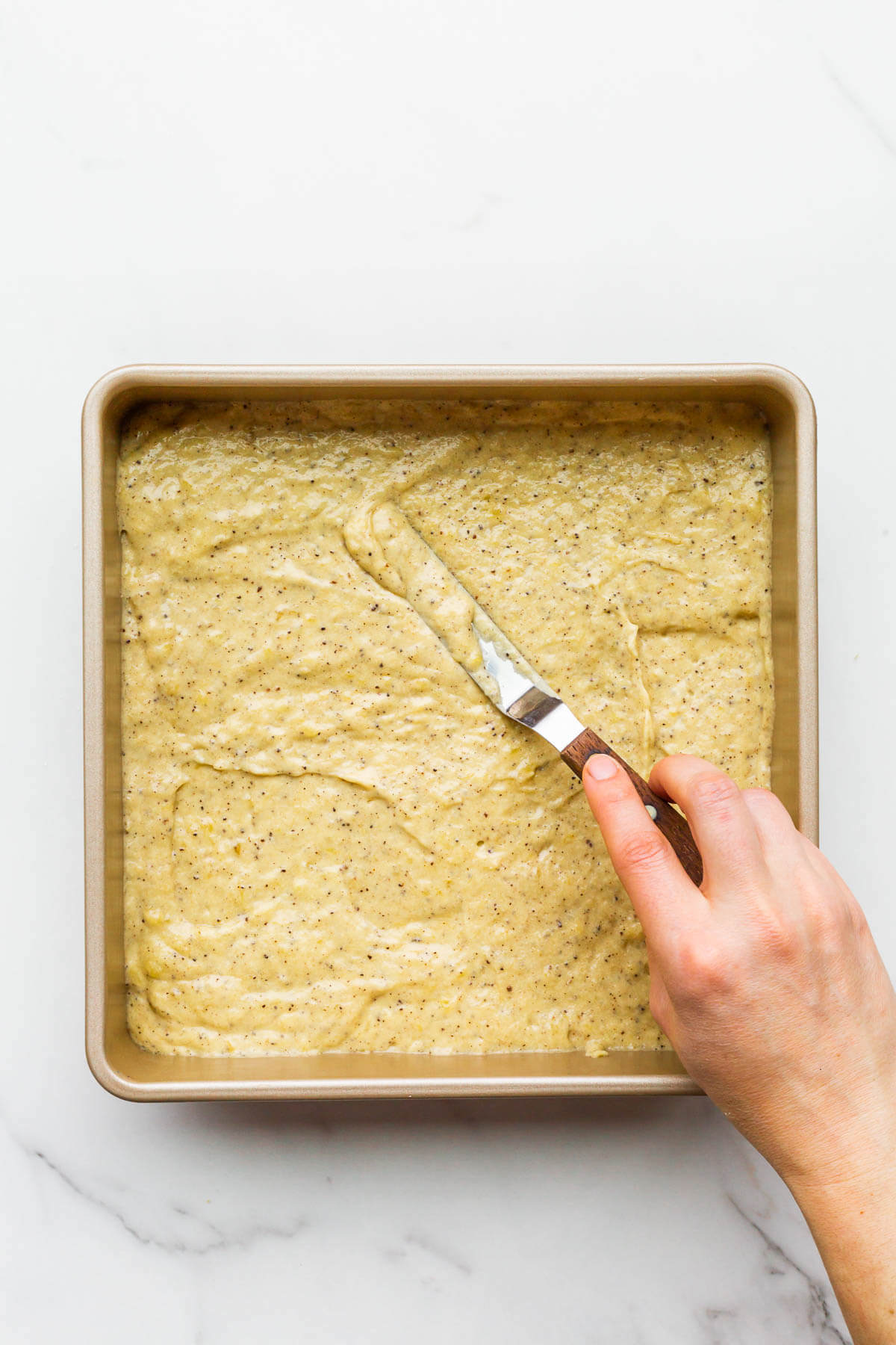 Smoothing banana cake batter in a square pan with a mini offset spatula to make a snack cake.