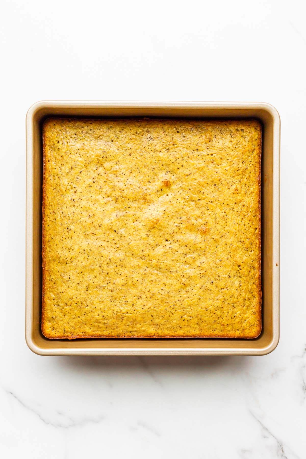Banana cake with golden brown edges pulling away from the sides of a square cake pan.