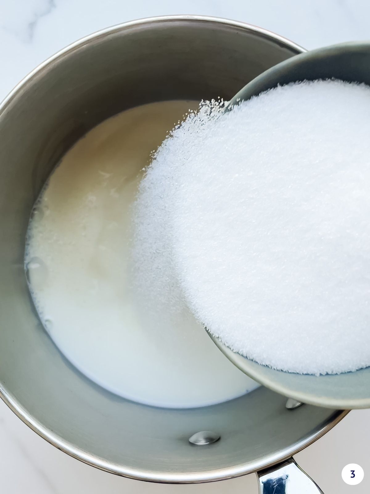 Pouring granulated sugar over a saucepan of milk to heat it on the stove to make custard sauce.