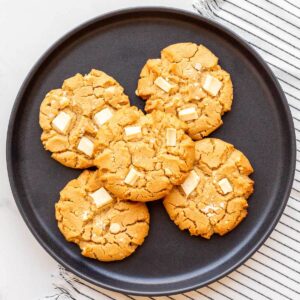 A black plate with 5 big peanut butter white chocolate chip cookies.