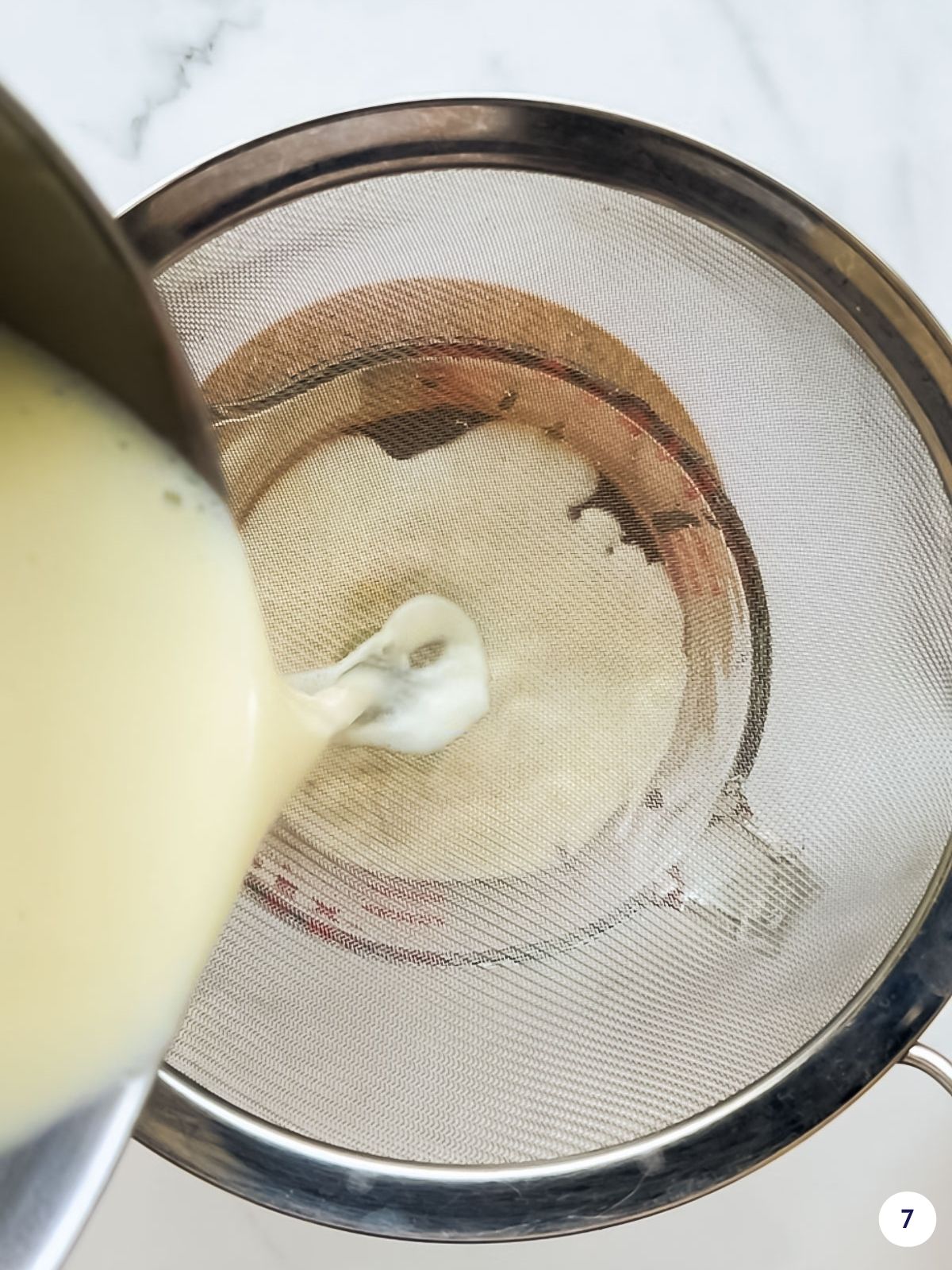 Straining custard sauce through a fine mesh sieve.