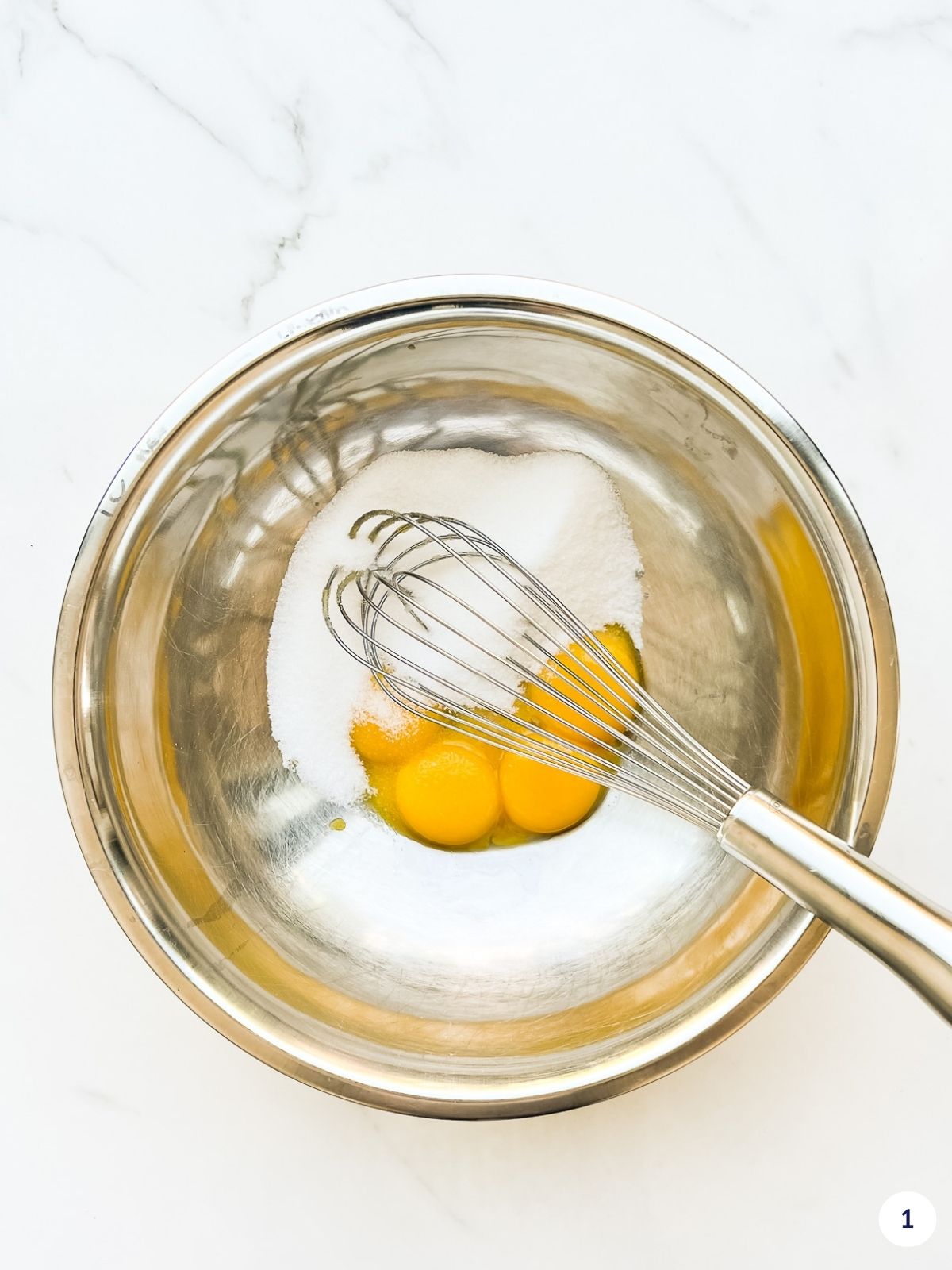 Egg yolks and sugar in a metal bowl with a whisk.