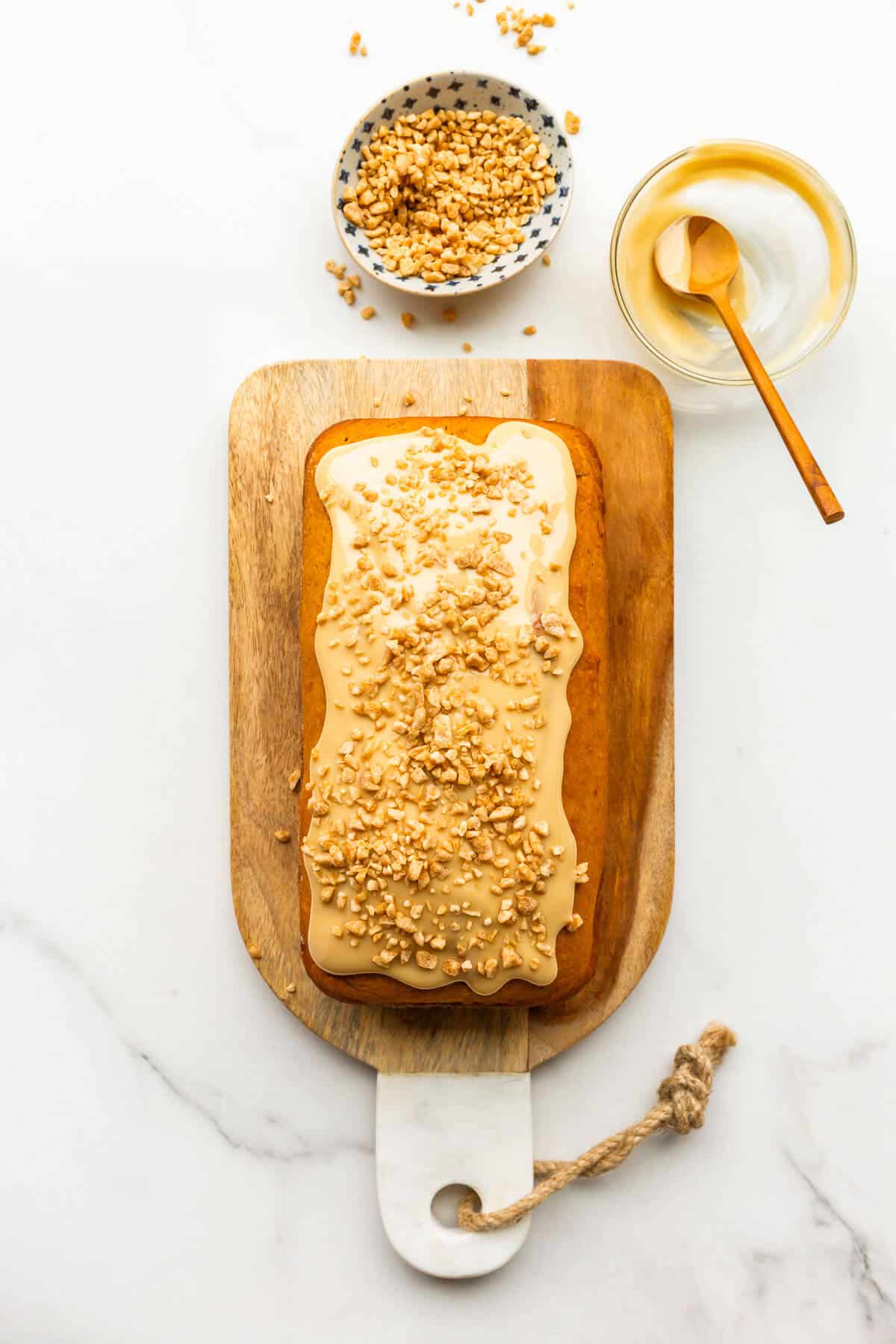 A pumpkin loaf cake on a cutting board iced with maple butter and garnished with maple flakes.
