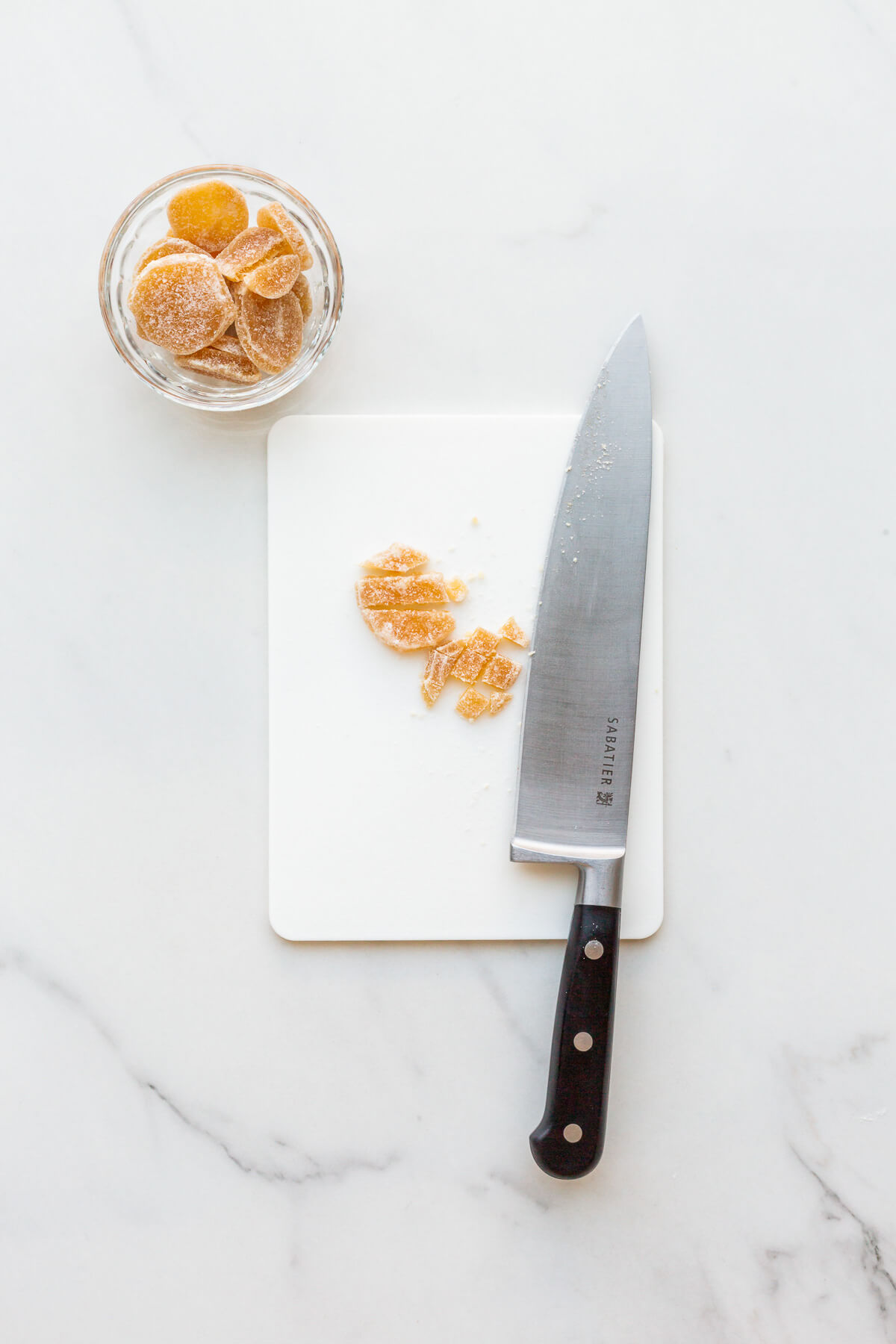 Chopping crystallized ginger with a chefs knife on a cutting board.