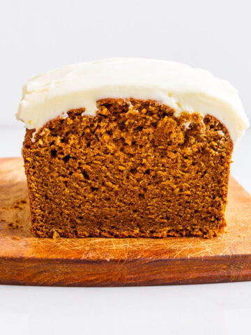 Whole wheat pumpkin loaf cake topped with a thick layer of cream cheese frosting on a cutting board.