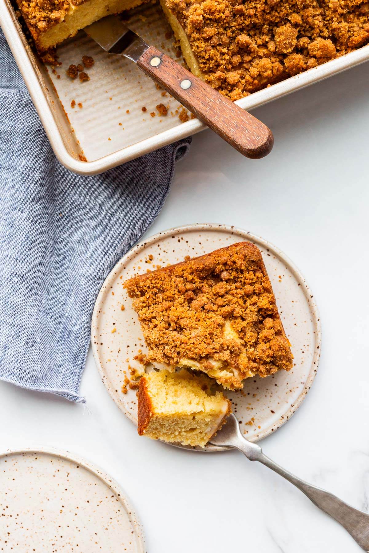 Taking a bite out of a square of apple coffee cake on a dessert plate.