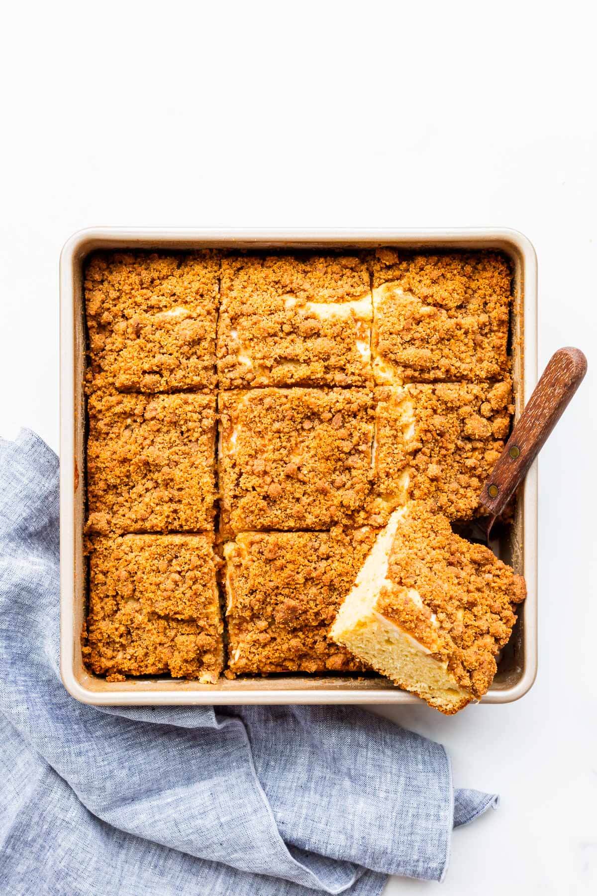 Serving apple crumb cake from a square cake pan with a mini offset spatula.