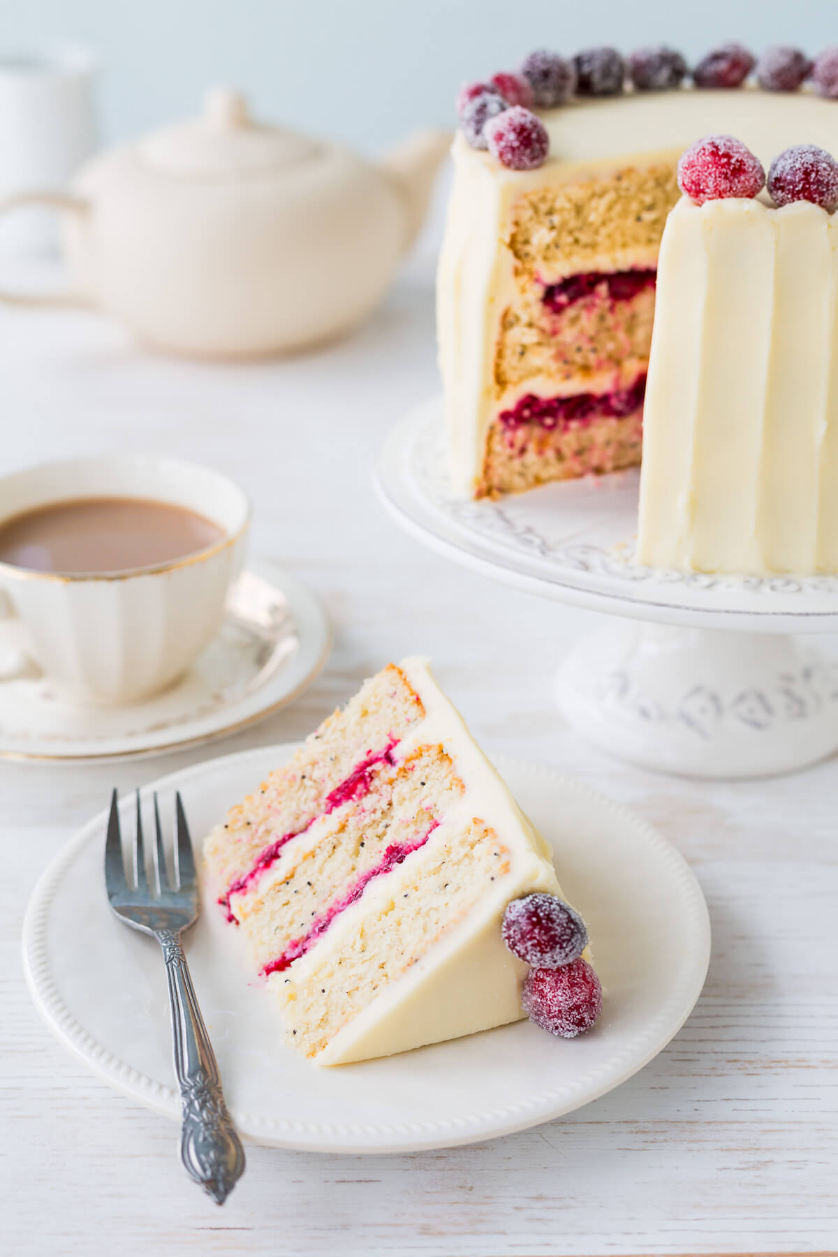 A slice of cranberry white chocolate cake served on a dessert plate with the layer cake in the background.