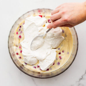 Spreading whipped cream over pastry cream and berries in a bowl to make trifle.