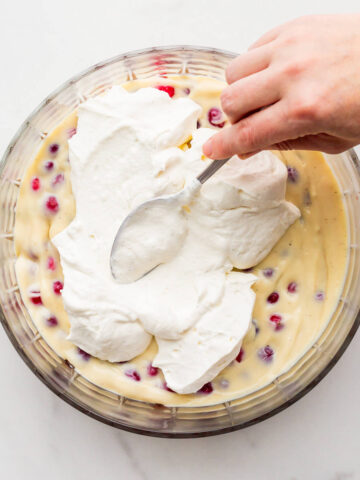 Spreading whipped cream over pastry cream and berries in a bowl to make trifle.