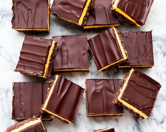 Nanaimo bars cut into squares and served on a marble surface.
