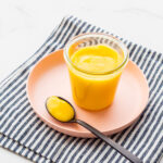 A jar of lemon curd set on a pink plate.