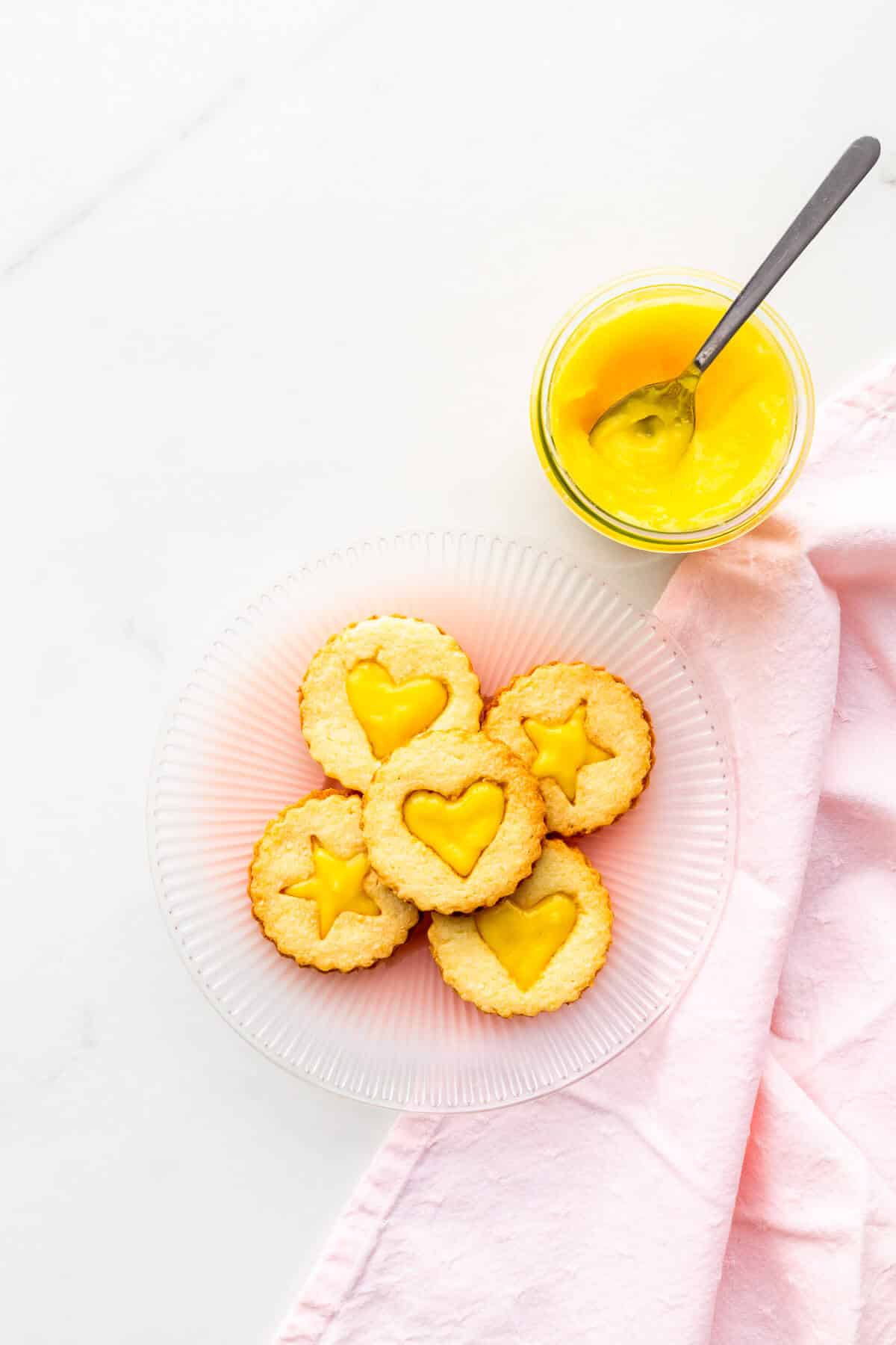 A plate of lemon-curd filled cookies with a jar of lemon curd on the side.