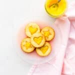 A plate of lemon curd-filled shortbread cookies with a jar of lemon curd on the side.