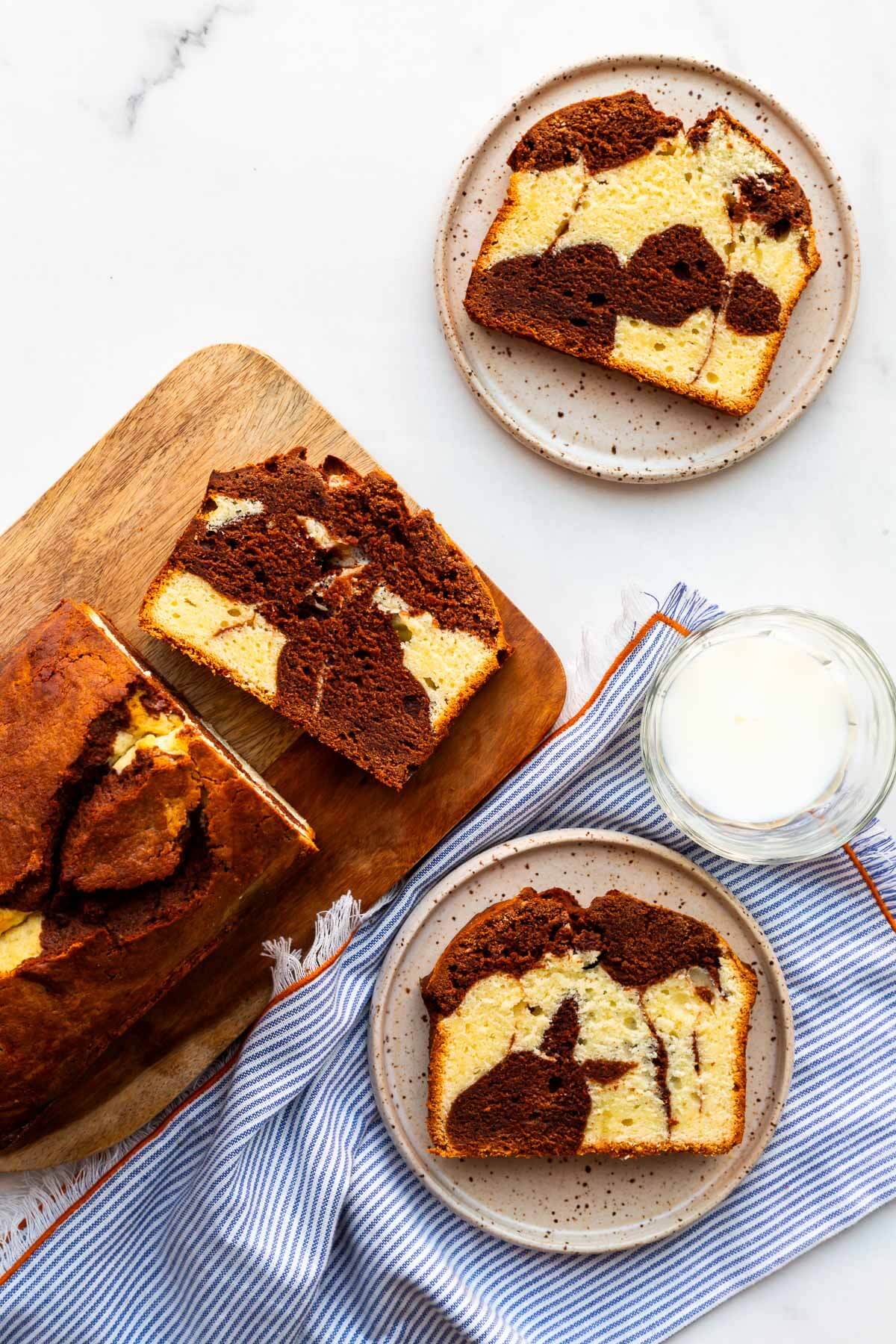 Chocolate and vanilla marble cake sliced on served on small dessert plates with a glass of milk on the side.