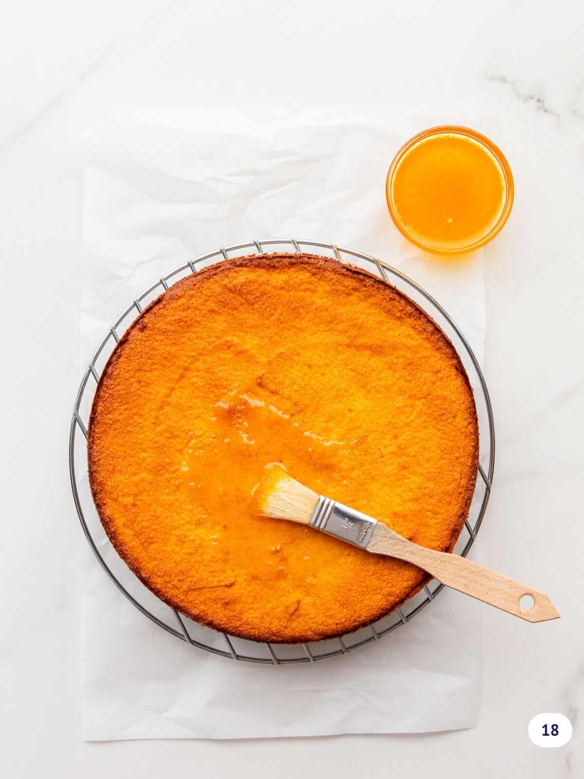 Brushing orange syrup on a cake set on a cooling rack.