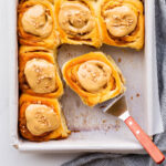 Serving maple cinnamon buns from the baking pan with a spatula.