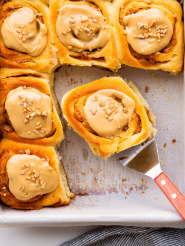 Serving maple cinnamon buns from the baking pan with a spatula.