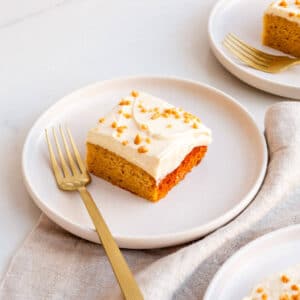 Squares of maple cake topped with whipped cream on dessert plates with forks.