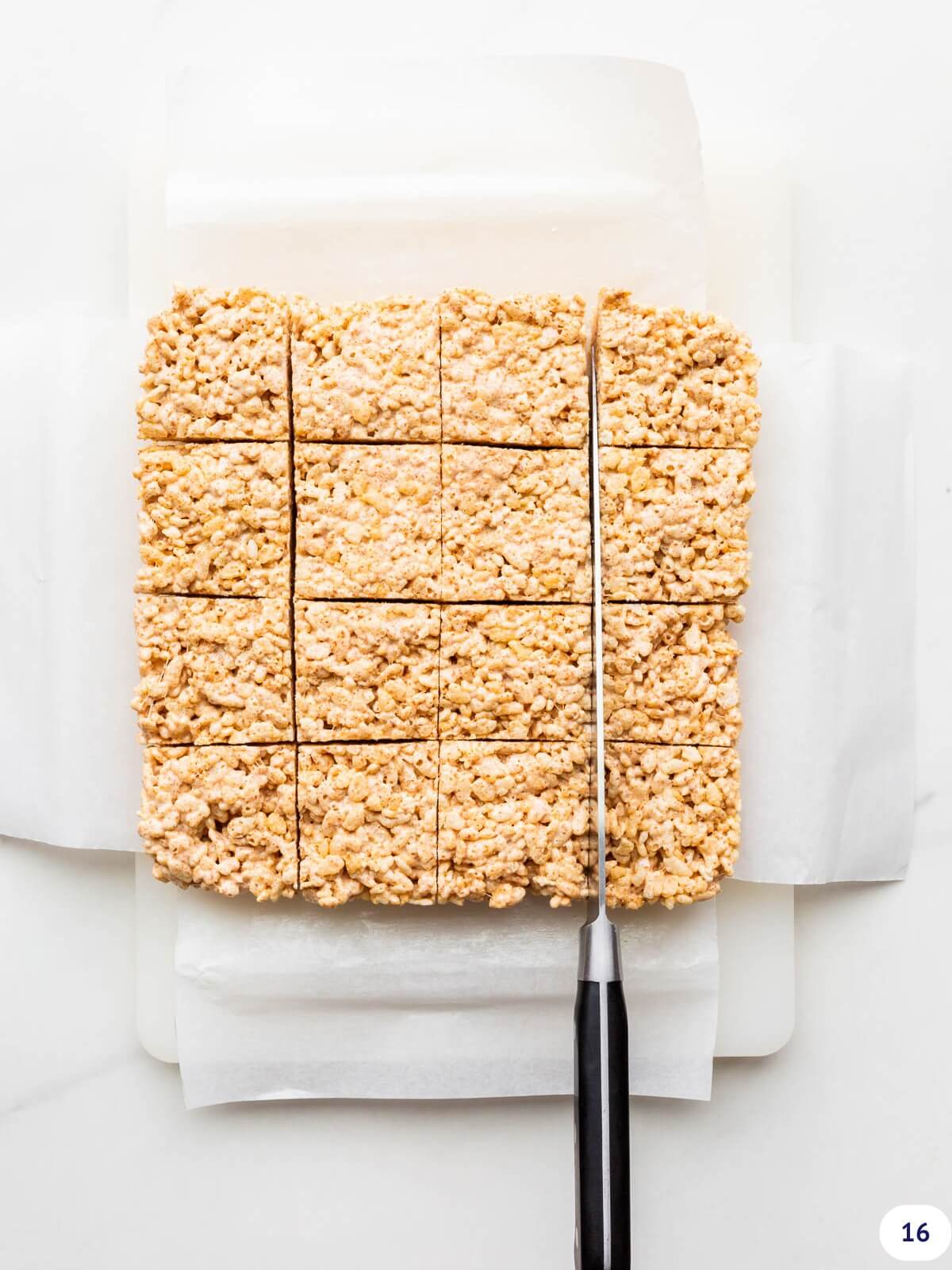 Cutting Rice Krispie treats into squares with a large chef knife on a cutting board.