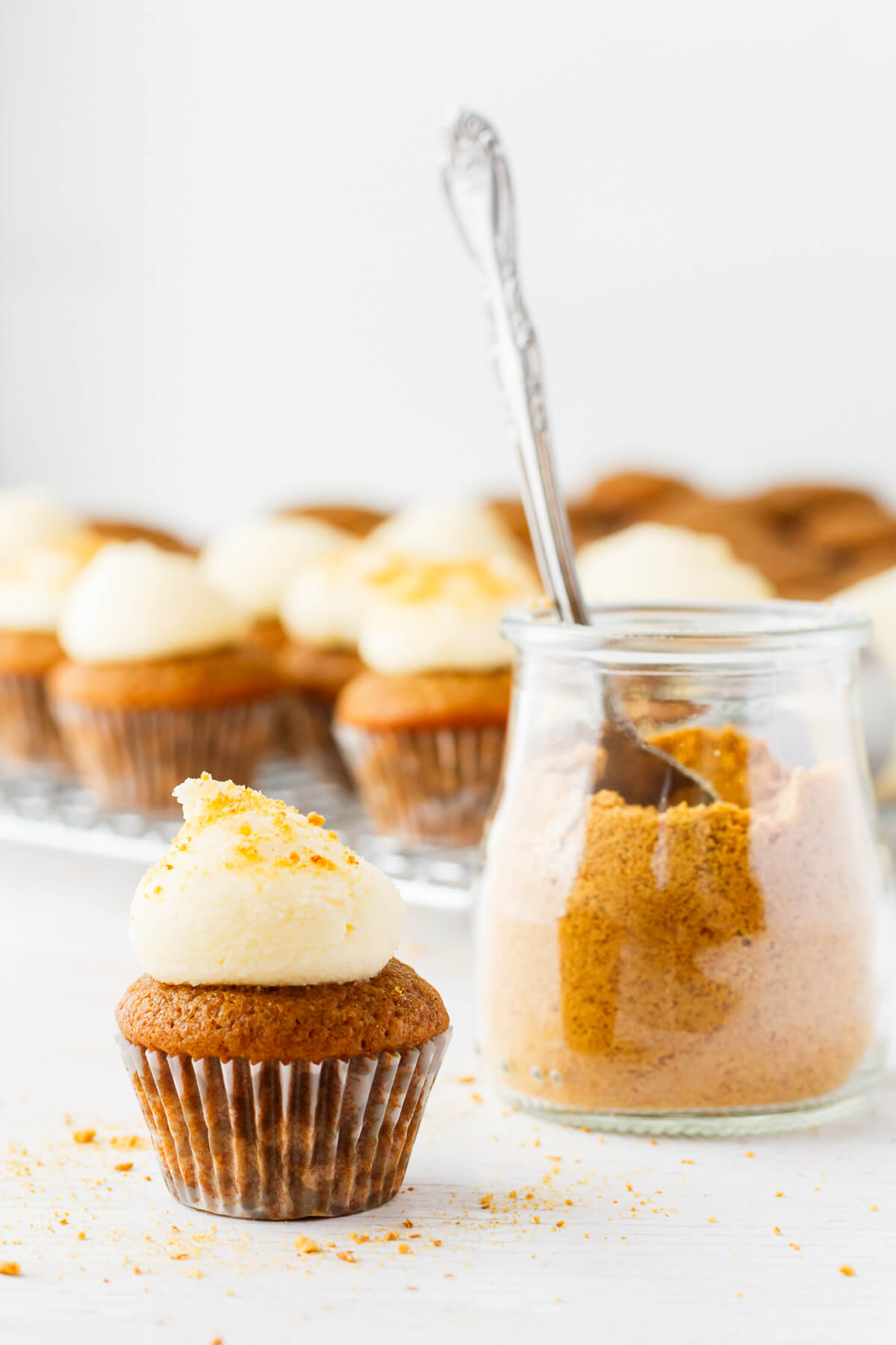 Topping apple cupcakes with cream cheese frosting and graham cracker crumbs.