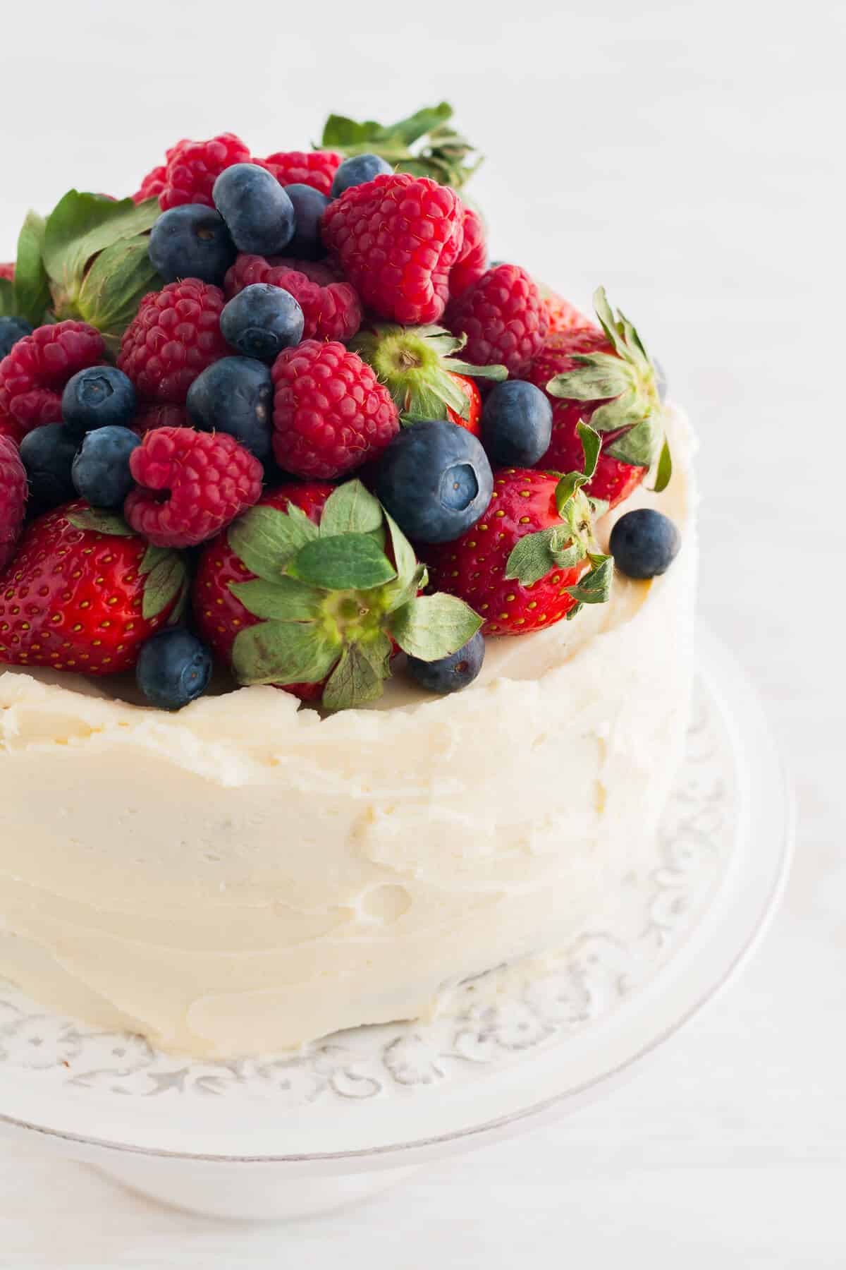 A layer cake topped with a mound of fresh berries on a cake stand.