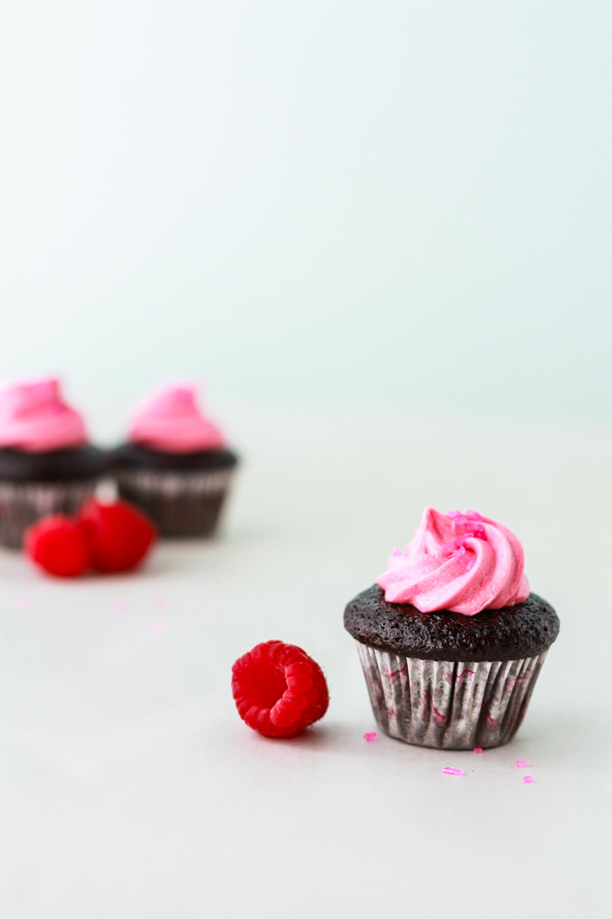 Mini dark chocolate cupcakes topped with pink raspberry frosting swirls.