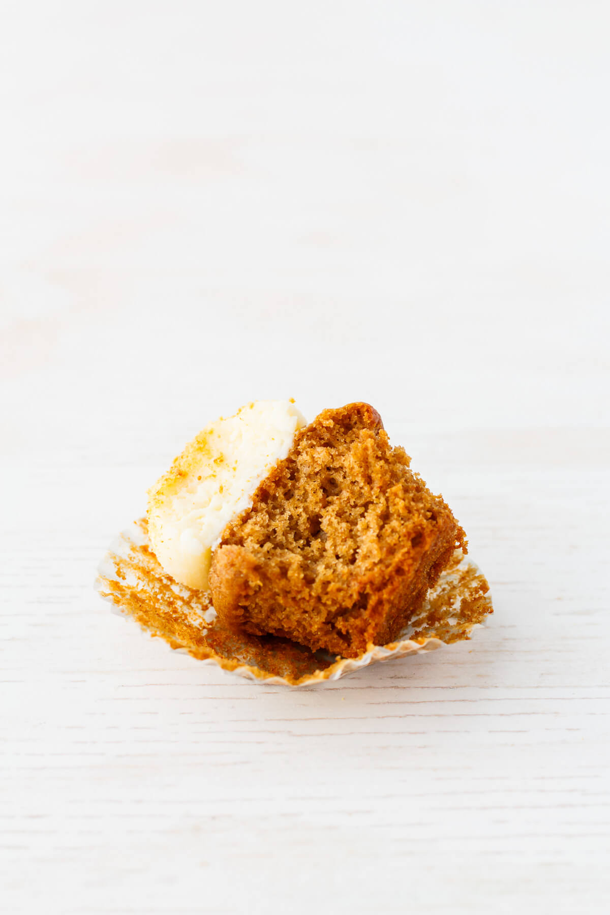 A apple spice cupcake that is topped with cream cheese frosting and cut in half.