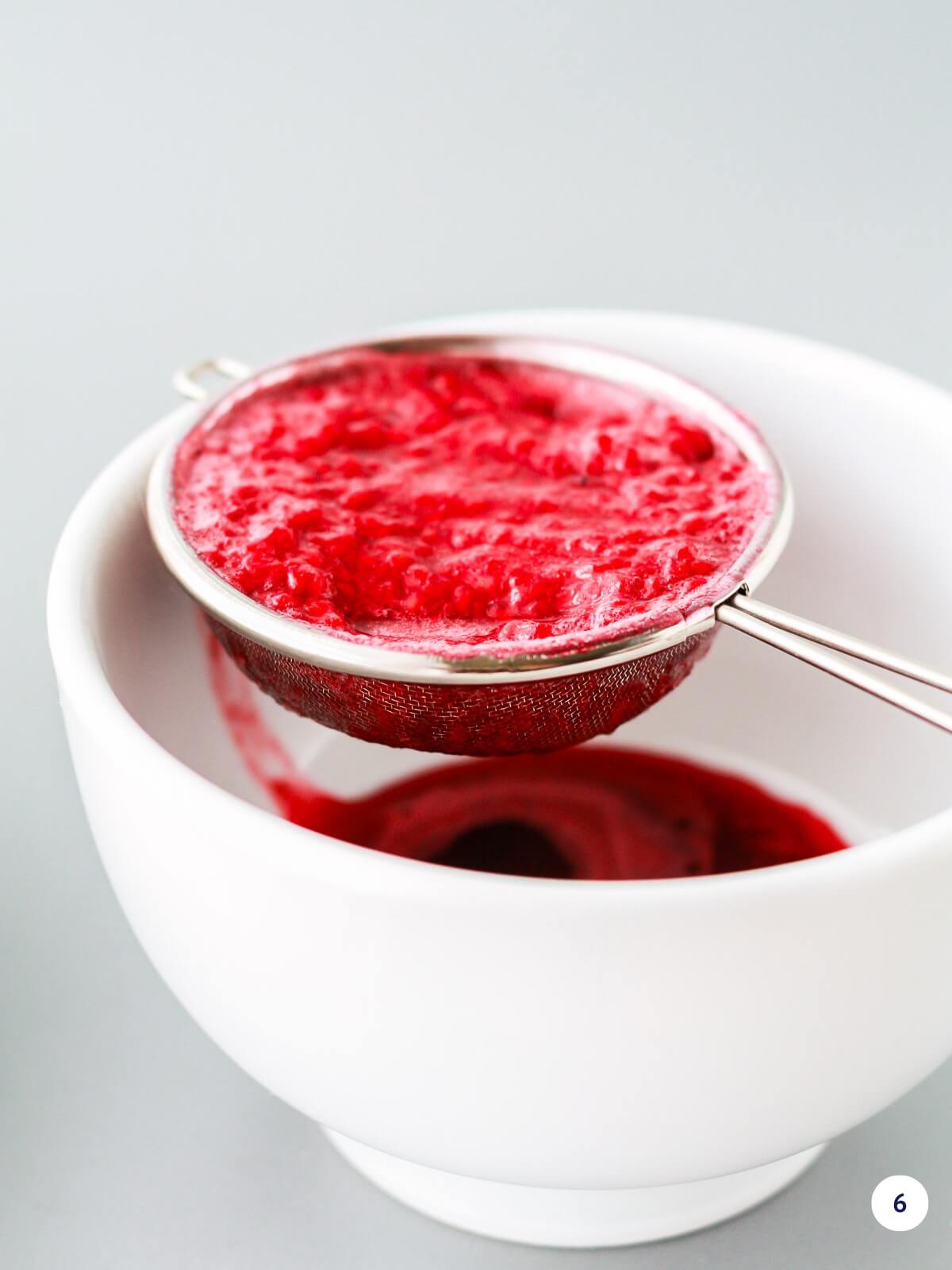 Straining raspberry purée to remove the seeds.