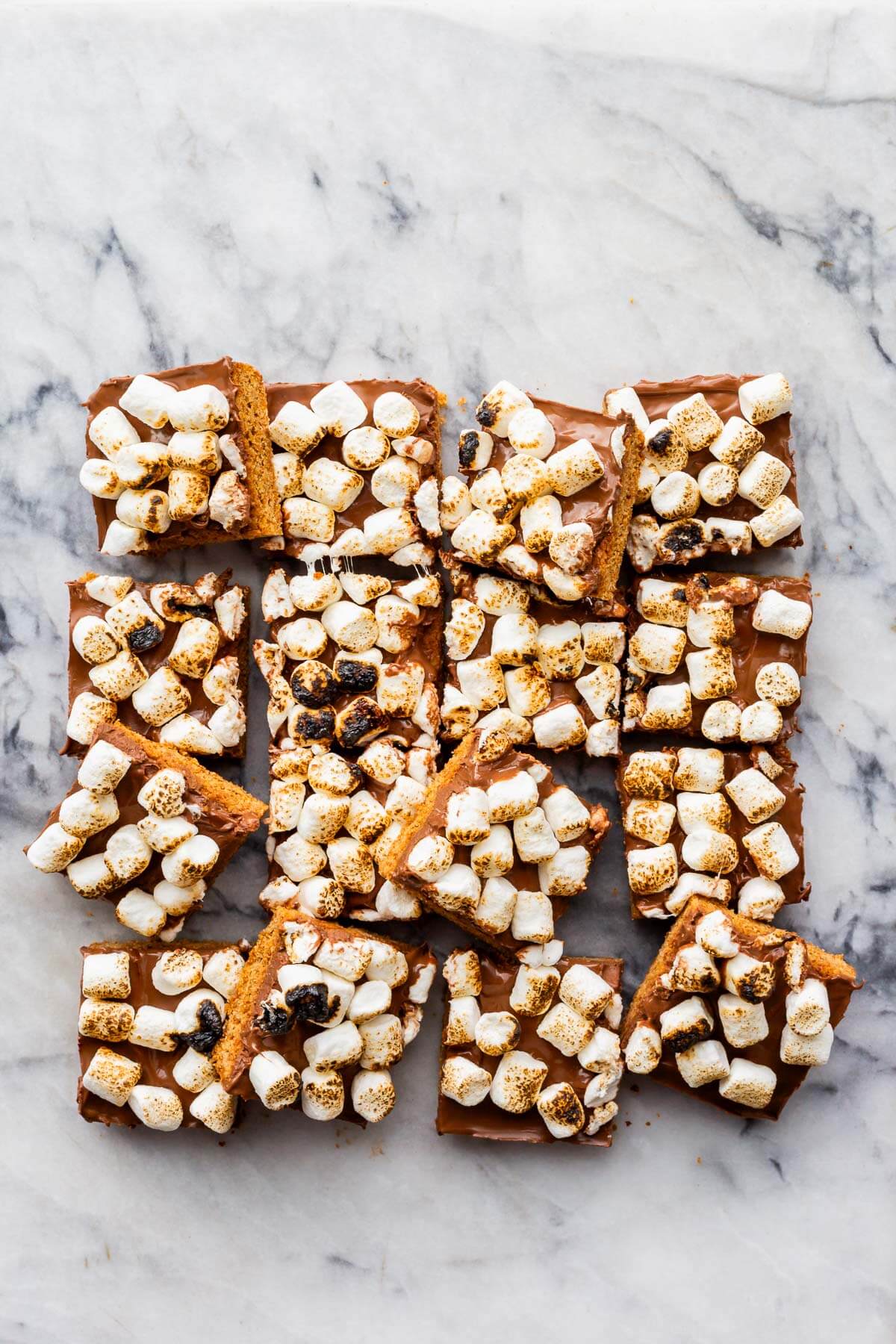 S'mores bars cut into squares made with a graham cracker cookie crust, milk chocolate filling, and toasted marshmallows on top.