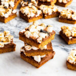A stack of s'mores bars with a graham cracker cookie crust, milk chocolate filling, and toasted marshmallows on top.