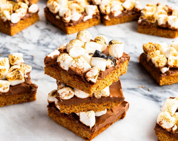 A stack of s'mores bars with a graham cracker cookie crust, milk chocolate filling, and toasted marshmallows on top.