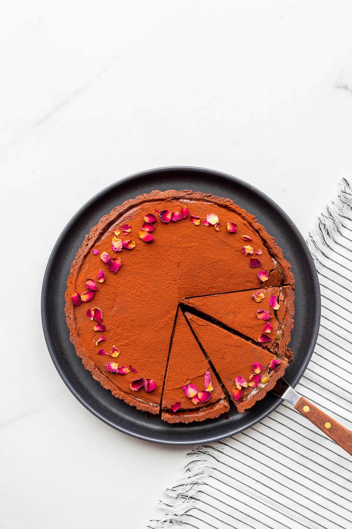 A chocolate ganache tart with a chocolate crust being sliced to serve it.