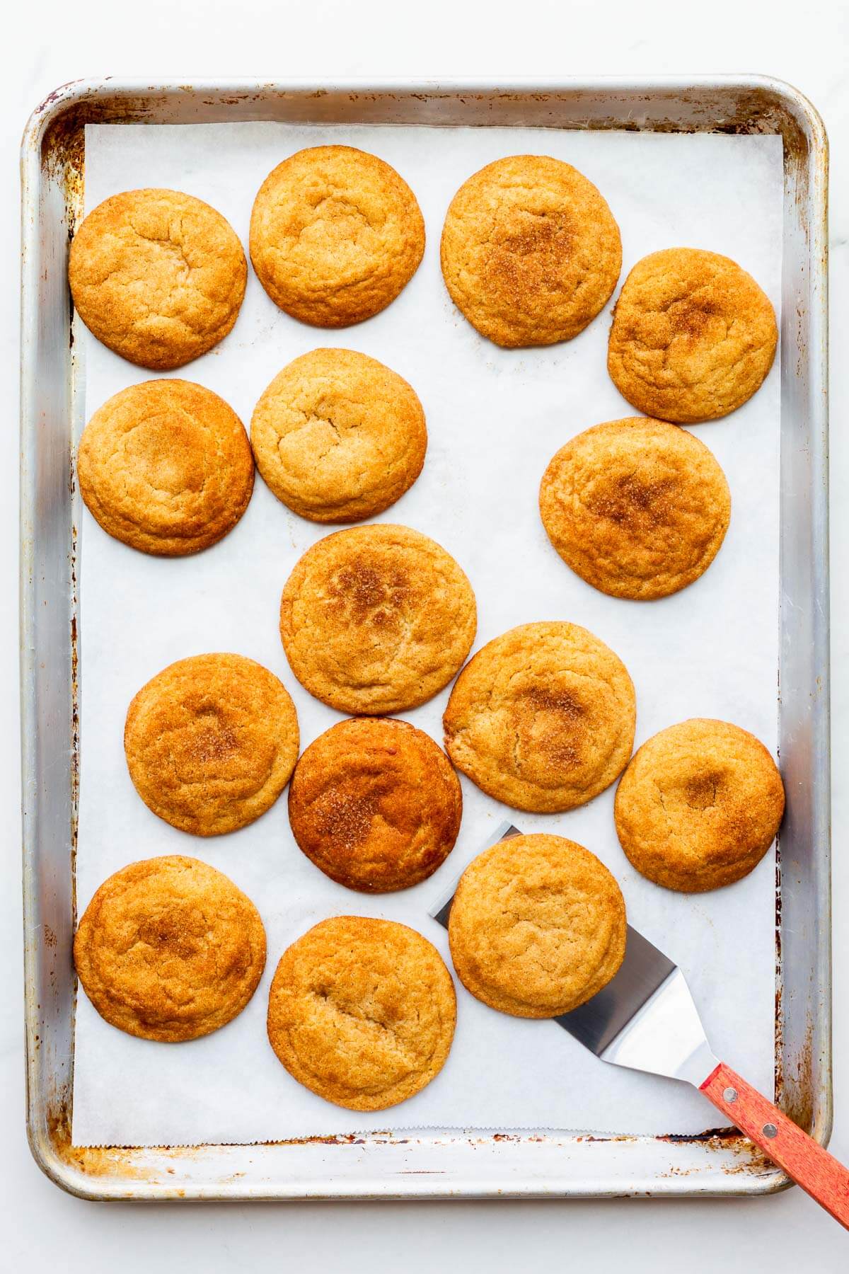 Using a spatula to lift freshly baked snickerdoodle cookies off a cookie tray.