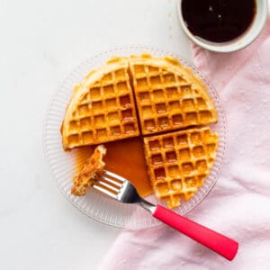 A plate with a sourdough discard waffle drizzled with lots of maple syrup.