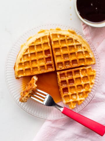 A plate with a sourdough discard waffle drizzled with lots of maple syrup.